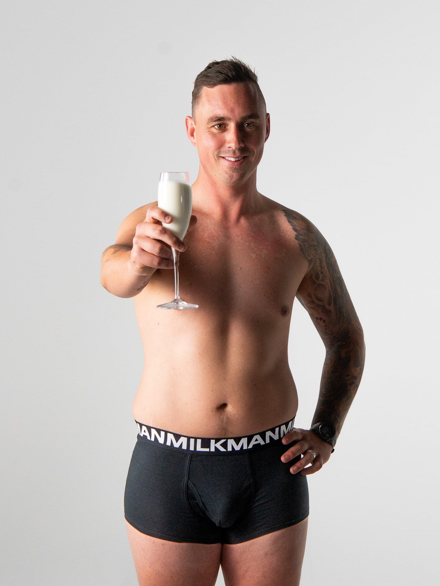 Man wearing black underwear with 'MilkMan' branding, holding a glass of milk.