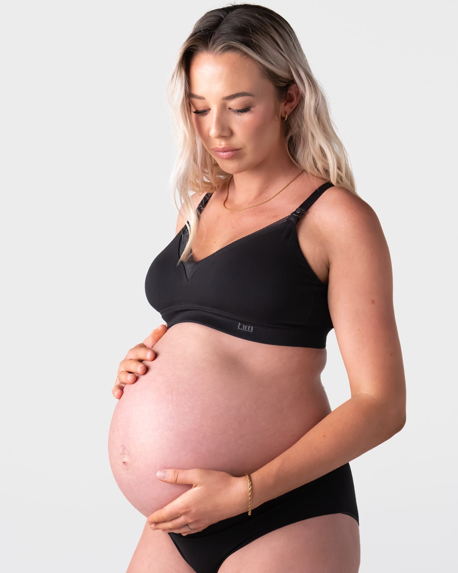 Pregnant model wearing the Hotmilk Caress FlexFit Nursing Bra in Black with matching briefs – three-quarter side view showing smooth cup shape, adjustable straps, and gentle wirefree support during pregnancy