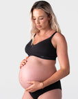 Pregnant model wearing the Hotmilk Caress FlexFit Nursing Bra in Black with matching briefs – three-quarter side view showing smooth cup shape, adjustable straps, and gentle wirefree support during pregnancy